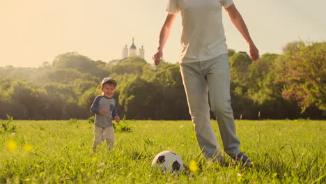 Ein-Junger-Vater-In-Einem-Weißen-T-Shirt-Und-Zwei-Söhne-Spielen-Bei-Sonnenuntergang-In-Der-Sonne-In-Zeitlupe-Fußball-Auf-Dem-Rasen